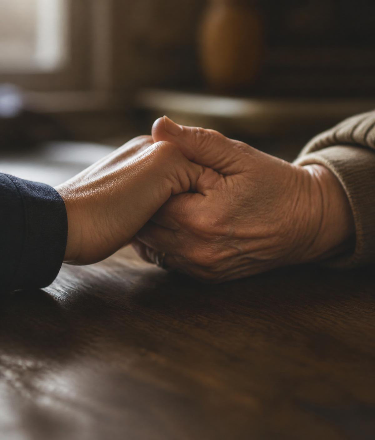 Two hands clasped in support across a wooden table